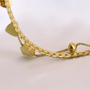 Macro shot of gold-plated flat snake chain with heart pendant and sliding bead on silk