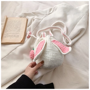 Detail of handmade knit bucket bag with rabbit ears and a red strawberry charm