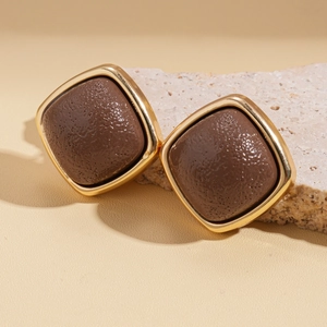 Macro detail of geometric square earrings featuring gold metal and brown textured leather inlay
