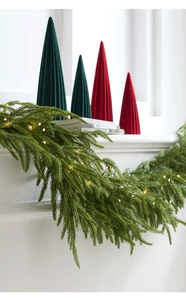 Detail of lush green artificial pine garland with warm LED lights on a white fireplace