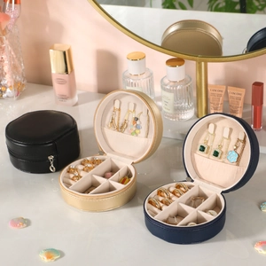 Three round portable jewelry boxes in black, gold, and blue with zipper closure