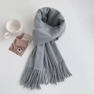 Detail of grey cashmere-like scarf with fringe tassels beside a ceramic mug and card