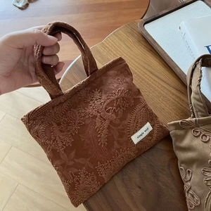 Detailed view of camel suede handbag with floral embroidery on wooden surface