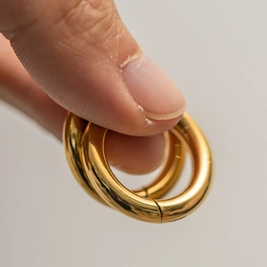 Macro shot of gold stainless steel hoop earring being held to show high-polished detail