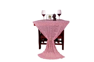 Detail of pink crinkled cheesecloth table runner draped on a dark wooden table texture