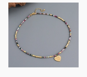 Detail of beaded necklace with heart-eye pendant and lobster clasp on grey surface