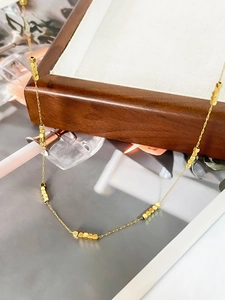 Detail of a minimalist gold square bead necklace draped over a wooden jewelry box