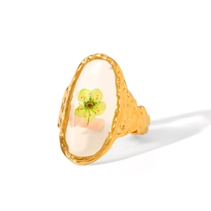 Detail of gold hammer-textured ring featuring a green dried flower in white resin