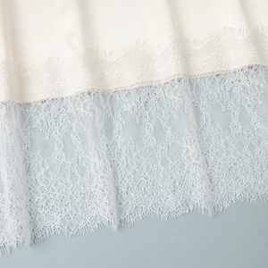 Detailed close-up of white satin fabric with delicate eyelash lace hem and fine stitching