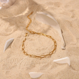 Minimalist 18K gold-plated paperclip chain anklet styled on beach sand with white accents