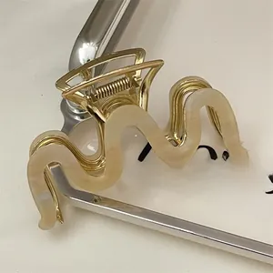 Close-up of wavy gold alloy and beige resin hair claw clip on elegant display tray