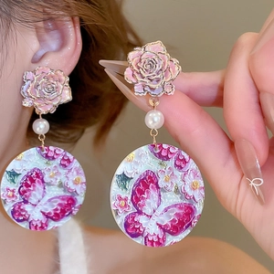 Close-up of retro floral drop earrings with pink resin roses and butterfly pendant charm