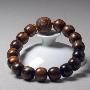 Macro shot of dark brown wooden prayer beads with a carved barrel bead and gold spacers