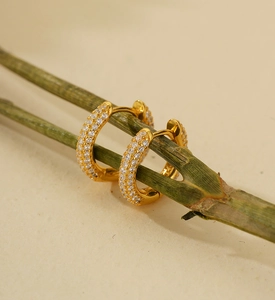 Macro shot of gold S925 sterling silver U-shaped hoop earrings with white zircons on a green stem