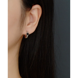 Close-up of a silver hoop earring with a black stone inlay worn by a female model