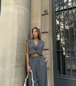 Detail of grey pinstripe vest and wide-leg trousers on model by a stone pillar
