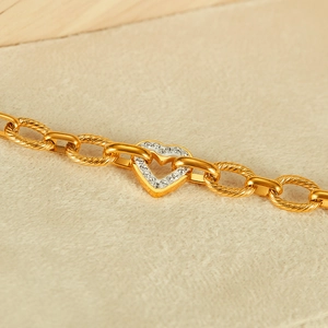 Close-up of golden chain bracelet featuring a heart link pave-set with white cubic zirconia