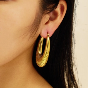 Close-up of chunky gold-plated stainless steel hoop earrings with textured spiral design