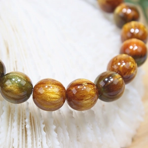 Macro detail of natural golden obsidian beaded bracelet with cat-eye effect on white coral
