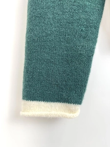 Detail of teal knit sweater cuff featuring white rolled edge contrast and soft texture