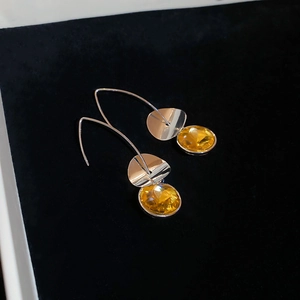 Macro detail of silver drop earrings featuring elegant yellow oval gemstones on black velvet