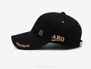 Close-up of black baseball cap with golden embroidery and square metal logo on the side