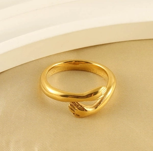 Detailed close-up of 18k gold-plated hugging hands ring on a beige silk background