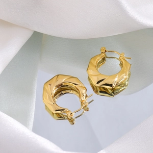 Macro shot of gold-plated twisted hoop earrings on silk fabric with reflective finish