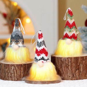 Close-up of glowing LED Christmas gnomes with colorful knitted hats on wooden base