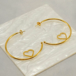 Minimalist gold heart hoop earrings in stainless steel on white marble background