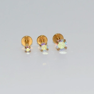 Detalle de tres piercings dorados de base plana con piedras de circonita redonda incrustada