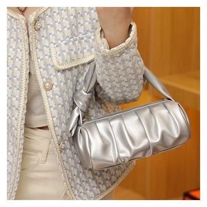 Detail of silver pleated barrel bag with knotted handle shown on model in tweed jacket
