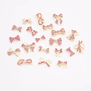 Detailed close-up of 19 assorted gold alloy and pink rhinestone bow nail art charms