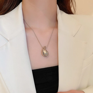 Polished silver teardrop pendant necklace worn by a model in a white blazer jacket