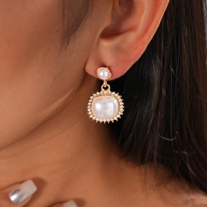 Detail of square pearl earrings with rhinestones and gold base on a female model