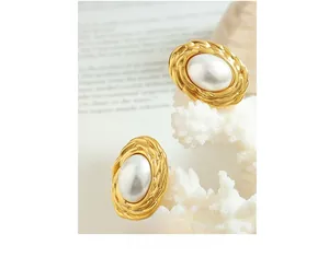 Detailed shot of gold French vintage pearl earrings with textured oval borders on coral