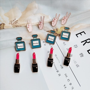 Close-up of alloy enamel pins showing lipstick, perfume bottle and V-sign gesture designs