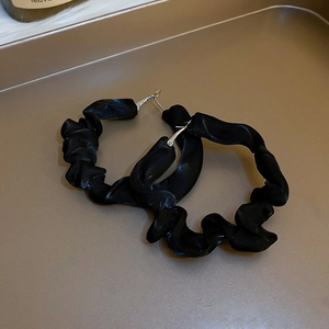 Close-up of black pleated fabric hoop earrings on a warm metallic jewelry tray