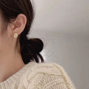 Gros plan d'une boucle d'oreille ovale en or mat portée sous une lumière naturelle