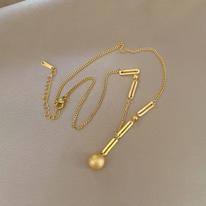 Minimalist titanium steel necklace with a gold frosted sphere pendant on beige fabric