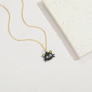 Close-up of golden necklace with a black cat pendant on a white marble background