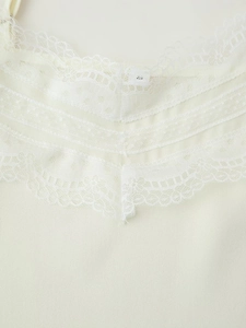 Close-up of intricate lace trim detail on the neckline of a cream camisole top