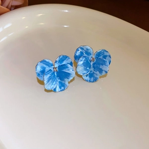 Gros plan de boucles d'oreilles fleurs en émail bleu et blanc avec cristal sur un plateau