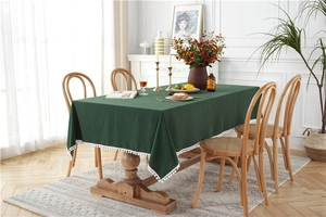 Detail of dark green cotton tablecloth featuring white pom-pom fringe on a wooden table