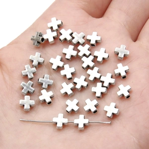 Detailed view of silver cross metal spacer beads for DIY jewelry making on a hand