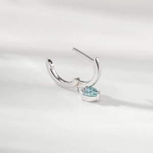 Silver hoop earring with light blue heart-shaped gemstone on soft grey background
