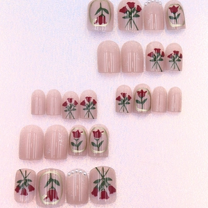 Detail of light pink press-on nails with red rose art and pearl accents for a retro look