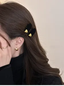 Dettaglio di fermagli per capelli a cuore nero floccato e anelli d'oro indossati da modella