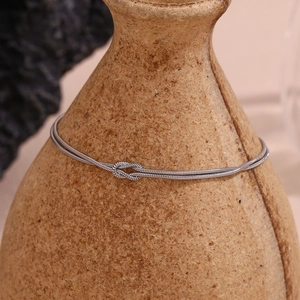 Close-up of a silver double-layer snake chain bracelet with a knot detail on a ceramic vase