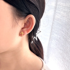Close-up of a minimalist gold airplane stud earring worn on a model's earlobe